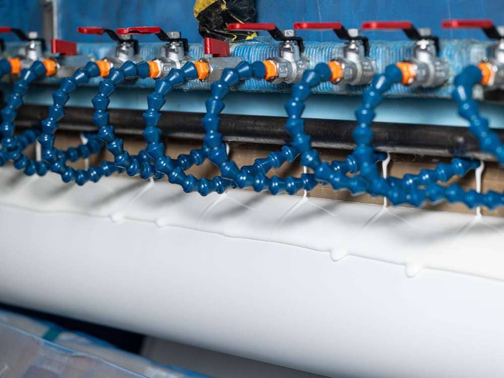 Sistema industrial aplicando adhesivo hot melt con boquillas de precisión sobre material en proceso.